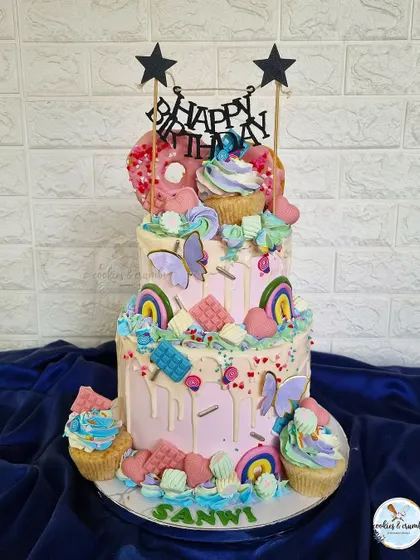 The final look of the two-tiered Candyland cake. It's a fun, overloaded design with donuts, cupcakes, chocolate bars, and rainbows, perfect for a first birthday.