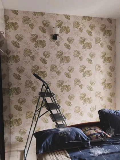 A bedroom with a subtle monstera leaf wallpaper, showing how it looks with a ladder still in the room during installation.