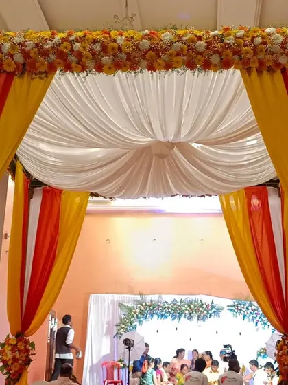 A classic wedding entrance with draped fabric in festive orange and yellow. The canopy is topped with marigolds, setting a traditional and welcoming tone for the celebration.