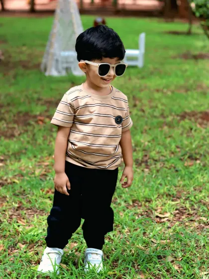 A cool toddler in sunglasses smiles during his second birthday outdoor shoot, capturing a candid and stylish moment.