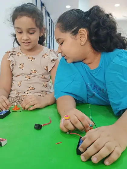 Two girls collaborate on building a simple circuit, learning about electricity together.