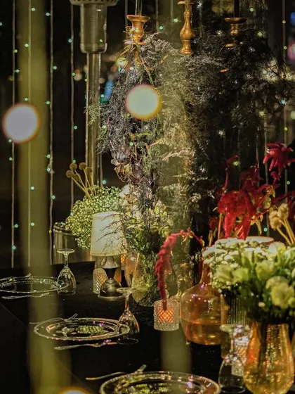 A tablescape detail showing a mix of florals against a backdrop of twinkling lights. The composition creates a sense of depth and enchantment, drawing the eye into the scene.