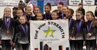 Our compulsory team celebrating with their District 6 Qualifier banner after a fantastic meet.