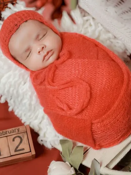 A close-up of the baby in the red swaddle, with a calendar block marking a special date.