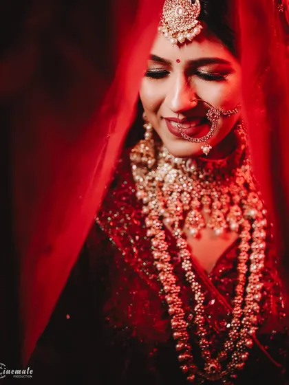 A dramatic close-up of the bride under a red veil, with lighting that highlights her smile and intricate jewelry.