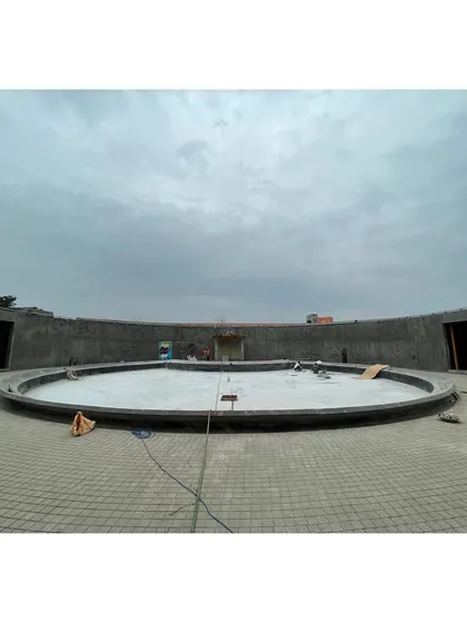 Workers inside the circular gallery during construction. This ground-level perspective shows the scale of the concrete structure before the final finishes and water feature were installed.