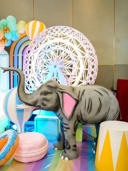 Whimsical decor from a pastel carnival theme, featuring a large elephant prop in front of a light-up ferris wheel.