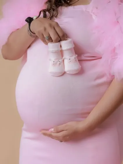 A close-up on the baby bump, with the mom-to-be in a pink ruffled gown holding tiny baby shoes.