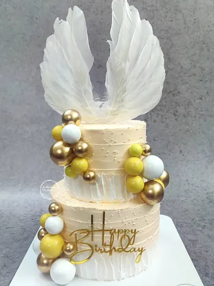 A grand two-tiered angelic birthday cake with large white feather wings.
