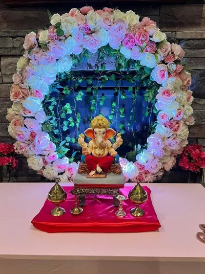 A floral ring lit from within creates a divine halo effect around the Ganpati idol. The backdrop of green vines adds a touch of nature to this modern and creative setup.