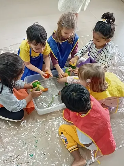 A group of children works together to wash plastic vegetables in a tub of water, a fun sensory and practical life activity.