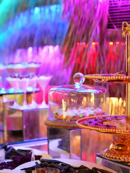 A vibrant dessert buffet under colourful lighting, featuring our tiered stands and glass-domed cloches. We create a visually dynamic and exciting dessert experience.