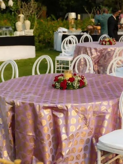 The guest tables were dressed in elegant pink and gold patterned tablecloths, with modern white chairs and a simple floral centerpiece, tying the whole look together.