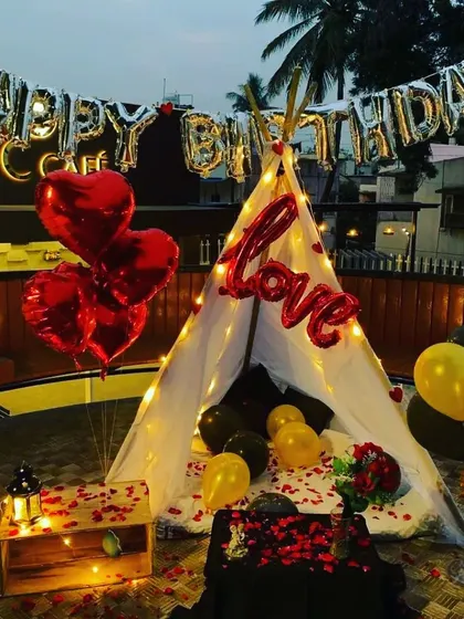 A cozy cabana tent setup on a rooftop for a birthday. This intimate setting includes "LOVE" foil balloons, fairy lights, and rose petals.
