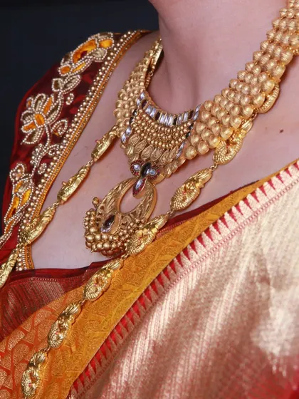 A close-up of a heavy, traditional gold necklace on a bride wearing a silk saree.