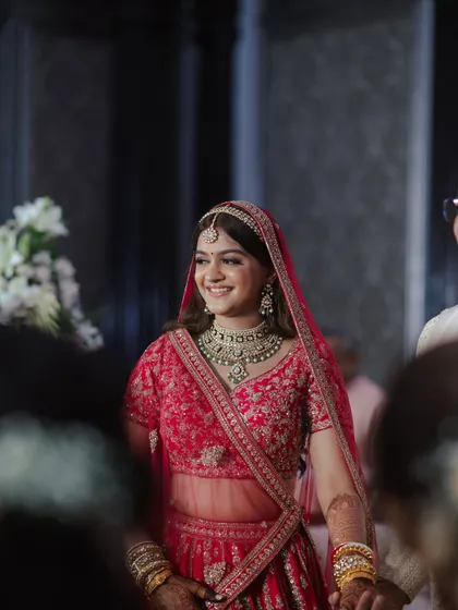A candid moment of the bride walking in, her smile lighting up the room. Her makeup is soft and radiant, complementing her traditional red lehenga beautifully.