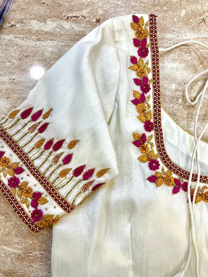 A beautiful off-white blouse with floral embroidery in shades of yellow and pink. The unique pattern on the sleeve resembles budding flowers, adding a fresh and elegant touch.