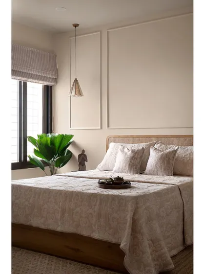 Another view of the minimalist guest bedroom. The clean lines of the wall moulding, the natural texture of the cane headboard, and the soft lighting create a warm and welcoming ambiance for visitors.
