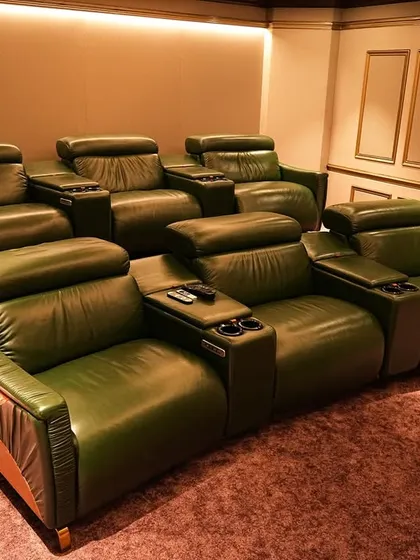 The olive-green leather recliners with wood and copper accents are the centerpiece of this opulent Chennai theater. The plush pink carpet adds a unique and luxurious touch.
