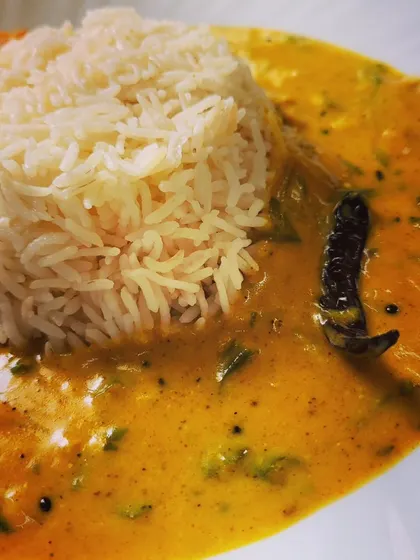 A close-up of the Kadhi, a smooth and creamy curry made from gram flour and yogurt, tempered with a whole dried red chili.