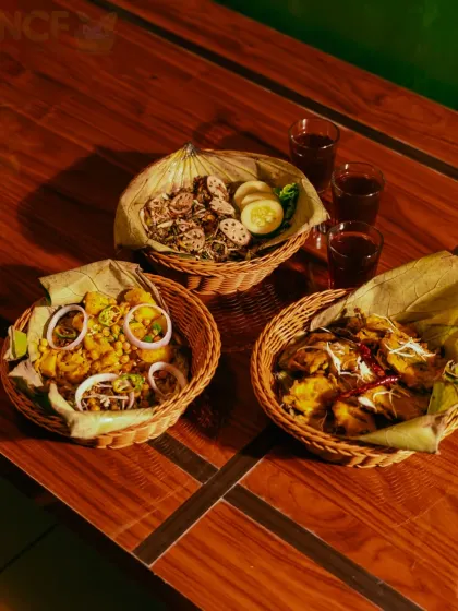 A traditional Manipuri snack combo featuring 'Singju', 'Bora', and 'Kelichana', served in woven baskets with 'Cha-ngang' (red tea).