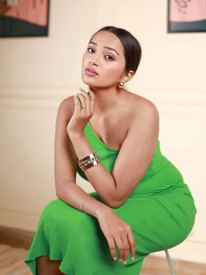 A full-body portrait that shows both the outfit and the model's comfortable presence. The simple stool prop and neutral background keep the focus entirely on her.