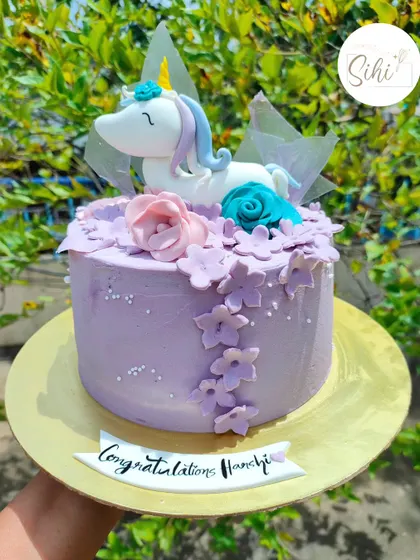 A whimsical unicorn cake in a lovely lavender shade. This design proves you're never too old for a bit of magic, featuring a sleeping unicorn surrounded by buttercream flowers.