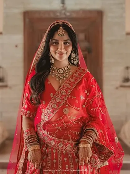 A regal portrait of the bride in a classic red saree. Her direct gaze and confident posture against a grand architectural backdrop create a powerful image.