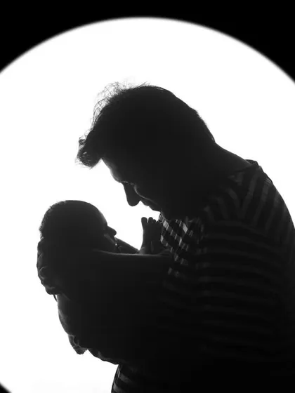 A father's silhouette as he holds his newborn baby up to the light. This black and white portrait is a powerful and artistic representation of a new bond.