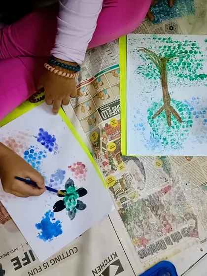 Children work together on their bubble art creations, using different colors and techniques to make trees and flowers. These collaborative art projects foster teamwork and shared imagination.