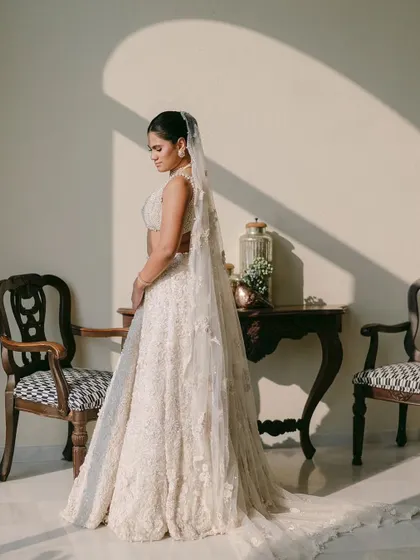 A bride in her stunning lehenga, with sunlight casting beautiful shadows on the wall behind her. This portrait is a beautiful play of light, texture, and graceful posture.