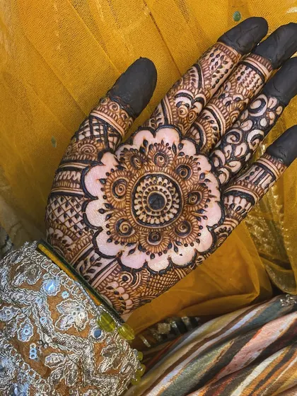 I love how this mandala design stands out against the bright yellow fabric. It shows the beauty of a central, bold pattern on the back of the hand, with detailed work on the fingers and a filled fingertip style.