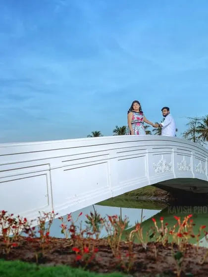 A grand, scenic pre-wedding photo of a couple on a white bridge, with palm trees and a clear blue sky creating a picturesque setting.