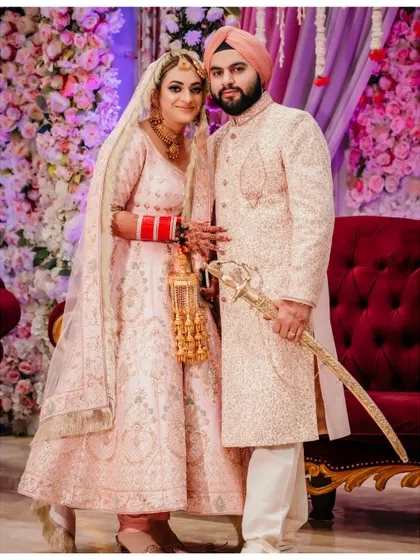 A classic portrait of a Sikh couple in soft pastel outfits. The floral backdrop and their gentle smiles create a romantic and elegant wedding day memory.