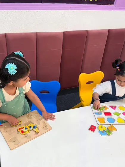 Two girls work on shape and animal puzzles together. Collaborative play is encouraged to help children develop social skills like sharing and communication while they learn.
