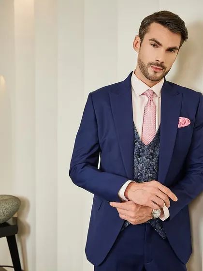 A three-piece ceremonial suit that combines classic Italian elegance with a modern twist. The rich blue suit is layered over a jacquard fabric waistcoat, with a pink shirt and tie adding a contemporary pop of color. This is sartorial style for the discerning man.