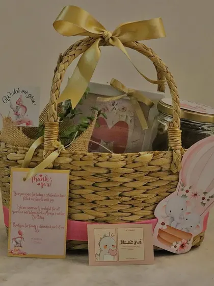 A premium first birthday return favor in a woven basket. This elephant-themed gift includes multiple jars of treats, a plant, and several personalized tags.