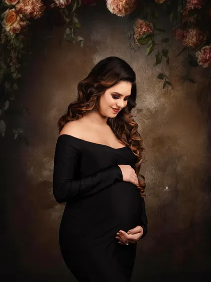 A classic and moody portrait against a painterly backdrop with floral elements. The client's simple black off-shoulder gown and serene expression create a timeless and artistic image.