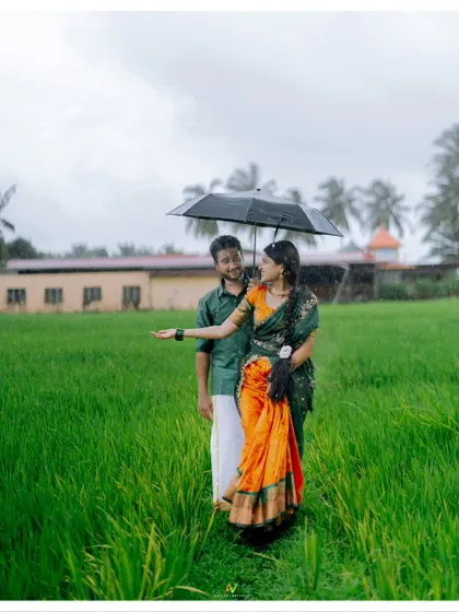 A romantic moment in the rain, with the couple sharing an umbrella in the middle of a green field.