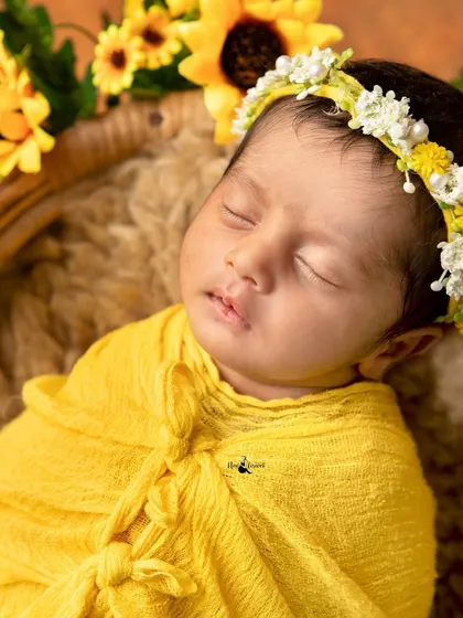 A close up portrait of a 14 day old newborn wrapped in a sunny yellow cloth, surrounded by sunflowers. Her peaceful expression is simply beautiful.