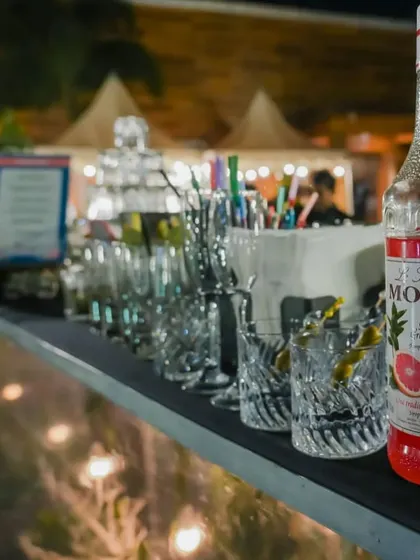 A bottle of Monin Pink Grapefruit syrup sits on the counter next to a line of crystal-cut glasses, showcasing the quality ingredients we use to craft our signature drinks.