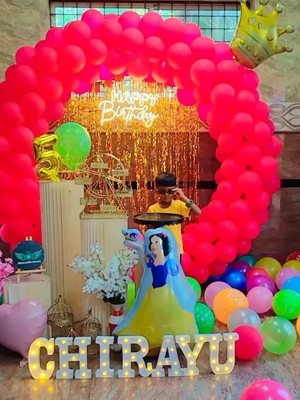 A bright and colorful birthday setup featuring a Snow White figurine and a vibrant red balloon ring.