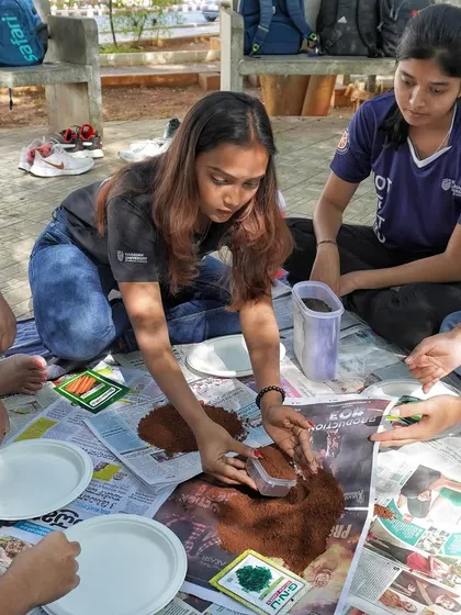 A group of students working together on the ground, mixing soil and making seed balls. This kind of collaborative, outdoor activity is great for student bonding.