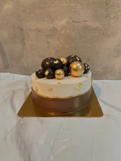 A sophisticated two tone cake with a chocolate base and white top, decorated with gold and black chocolate spheres.