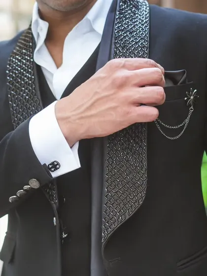 A close-up on the textured lapel and pocket square detail of the black suit.
