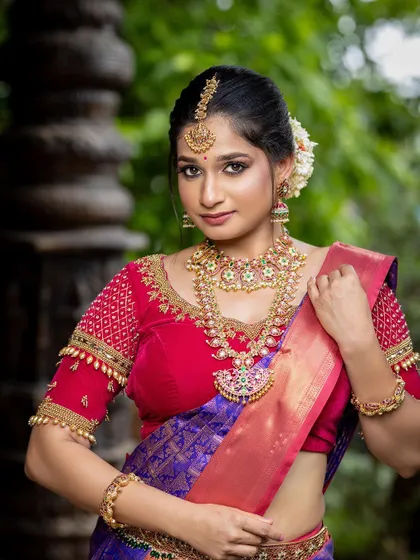 A beautiful portrait of a bride in a red and purple silk saree, set against ancient temple pillars. This is a perfect example of a timeless pre-wedding shoot look.