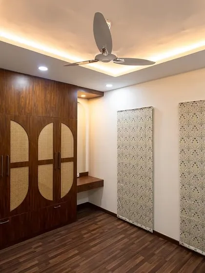 A bedroom from Nisha and Arun's home, featuring a beautiful wardrobe with semi-circular rattan-finish doors. The wooden flooring and patterned wall panels add texture and warmth to the space.
