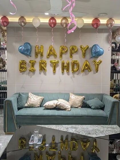 Even a simple living room can be transformed for a celebration. This classic setup includes "Happy Birthday" foil letters on the main wall, with helium balloons in rose gold, pink, and white floating on the ceiling to fill the space with color.