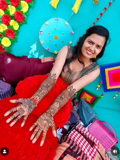 A happy client posing against a colorful backdrop, her full-arm mehndi designs on full display.