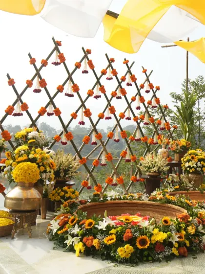 A beautiful Haldi setup by the lake, featuring a bamboo lattice backdrop adorned with marigolds and two large brass urlis filled with flowers for the ceremony.